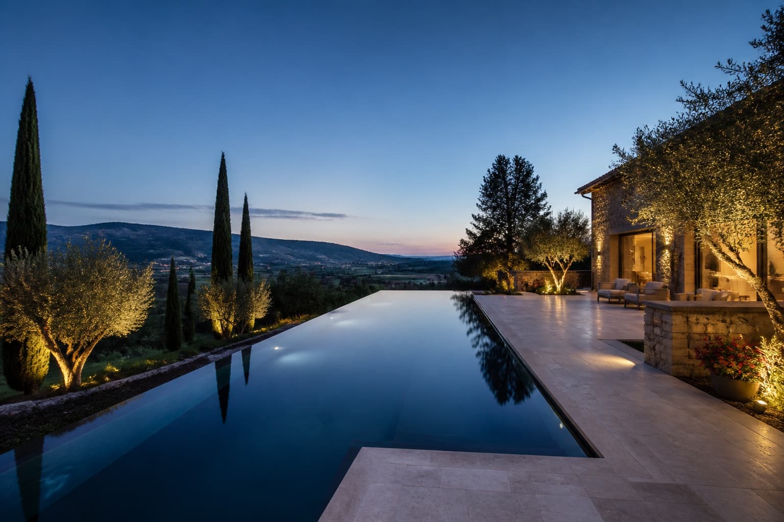 Vanishing-edge pool at dusk with limestone deck and warm house light